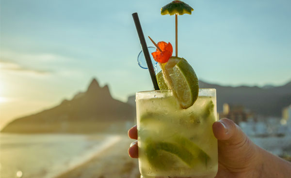 Ein Glas mit einem mit Schirmchen verzierten Capiriniha Cocktail am Strand