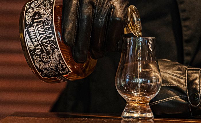 Guy Fawkes Whisky wird in ein Glencairn eingeschenkt, von einer mit schwarzen Lederhandschuhen, mysteriösen Figur