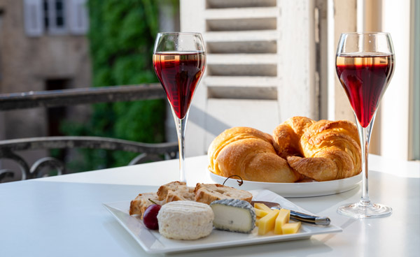 Zwei Kir Royal Cocktails zu Croissants und Käse auf sommerlicher Terrasse oder Balkon