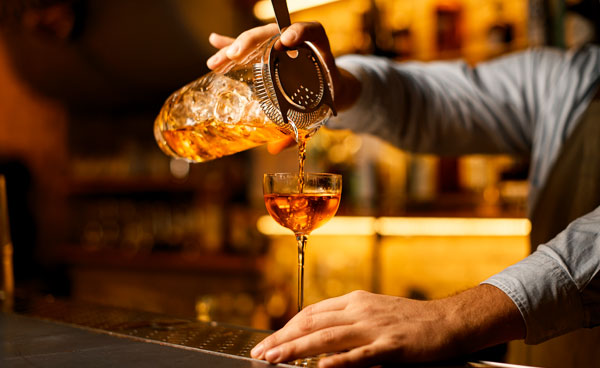 Bartender gießt Drink aus Shakerbecher mit einem Strainer ein